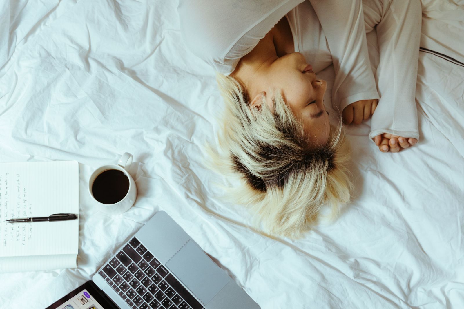 Someone asleep in bed beside a laptop and coffee, while their payments run on schedule
